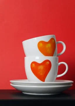 Two white tea cups with painted red hearts on red background, selective focus Stock Photos