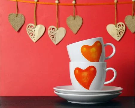 Two white tea cups with painted red hearts and wooden hearts on a string on r Stock Photos
