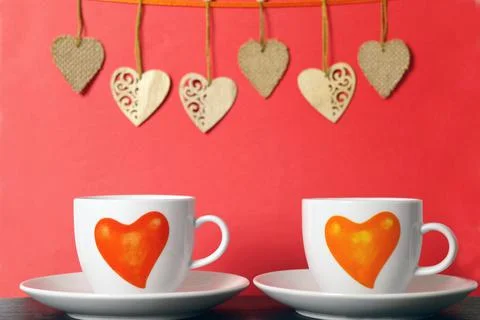 Two white tea cups with painted red hearts and wooden hearts on a string on r Stock Photos