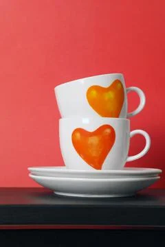 Two white tea cups with painted red hearts on red background, selective focus Stock Photos
