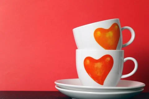 Two white tea cups with painted red hearts on red background, selective focus Stock Photos