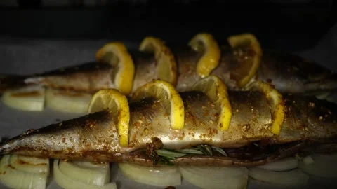 Two whole appetizing fish with lemon on onion rings on parchment in the oven Stock Footage 233599469
