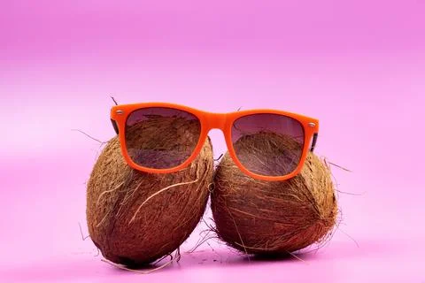 Two whole coconuts and orange glasses on a pink background. Stock Photos