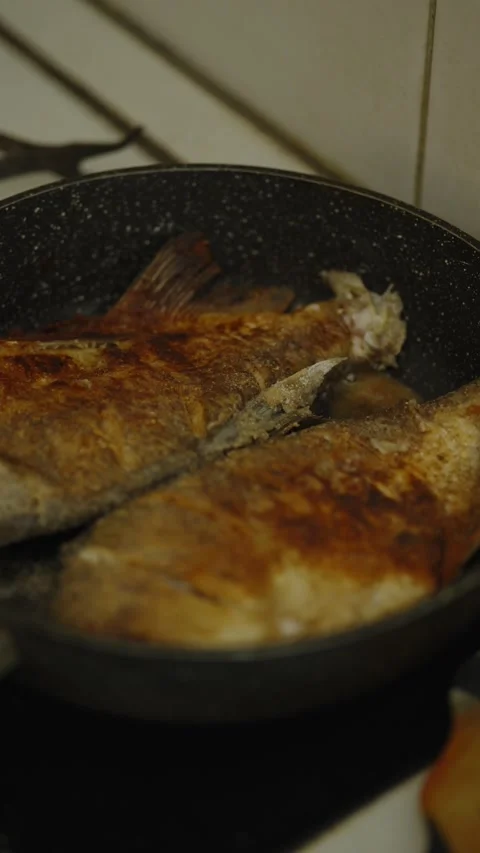 Two whole fish frying in a black nonstick frying pan Stock Footage 337760977