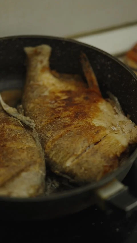 Two whole fish frying in a black nonstick frying pan Stock Footage 337760978