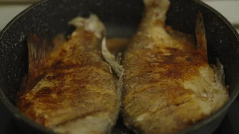 Two whole fish frying in a black nonstick frying pan Stock Footage 337760979