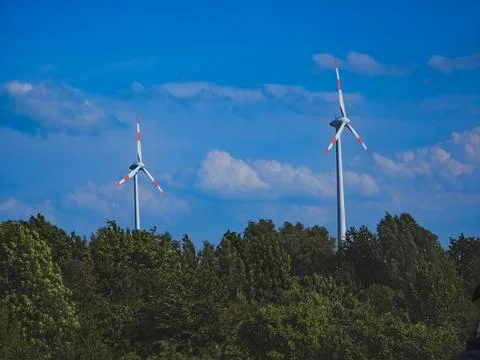 Two wind turbines behind the forest under blue sky, Stock Photos