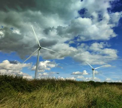 TWO WIND TURBINES IN THE FIELD WITH CLOUDY SKY Stock Photos