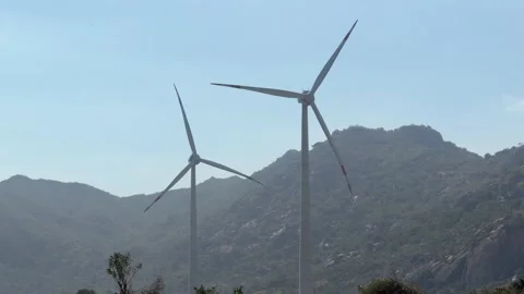 Two wind turbines rotate side by side, their blades cutting through the air with Stock Footage 328300717