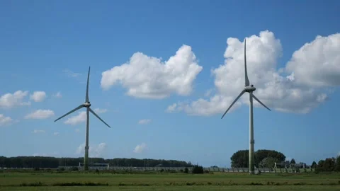 Two wind turbines turning in open green field under blue sky with clouds Stock Footage 319914334