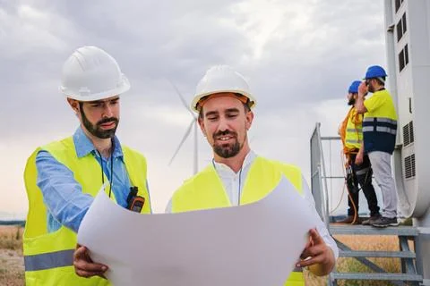 Two windmill engineers looking a blueprint with the plan of the construction of Stock Photos