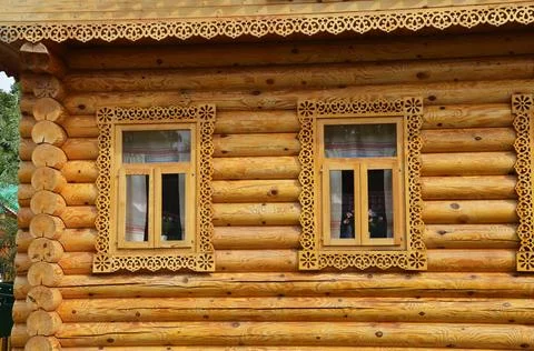 Two windows with carved frames of a brown wooden house. Wooden log village ho Stock Photos