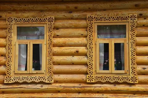 Two windows with carved frames of a brown wooden house. Wooden log village .. Stock Photos