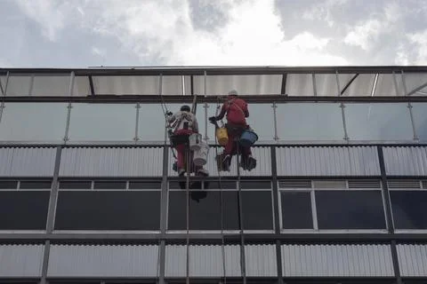 Two windows washers doing his job at high modern skyscraper with cloudy sky. Stock Photos