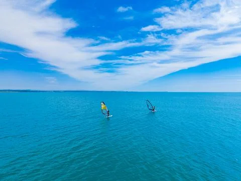 Two windsurfers glide over the calm water under a clear blue sky with small w Fotos Stock