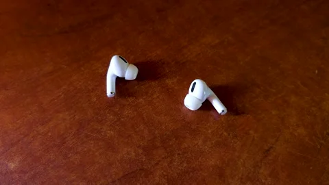 Two wireless earbuds placed side by side on a surface in an indoor environment. Video stock 323961401