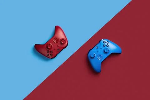 Two wireless gamepads red and blue lie on a background of opposite color.  Co Stock Photos