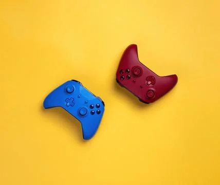Two wireless gamepads red and blue lie on a yellow background.  Confrontation Stock Photos