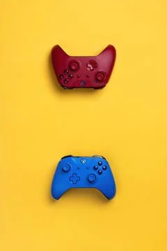 Two wireless gamepads red and blue lie on a yellow background.  Confrontation Stock Photos