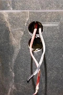 Two wires are securely connected to a small hole in the wall Foto stock