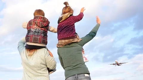 Two woman with a child on shoulders joyfully greeted a plane landing by airport Stock Footage