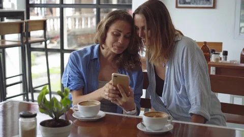 Two woman sharing coffee using smartphone in cafe Stock Footage 101291907