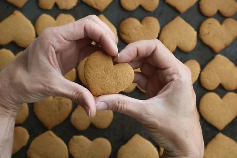 Two woman's hands forms heart shape, holding heart cookie on cookies background Stock Photos
