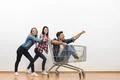 The two women and a man fun with a shopping cart on a white wall background Photo