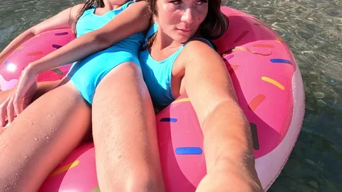 Two women in blue swimsuits float on a pink donut-shaped inflatable ring in the Stock Footage 280903229