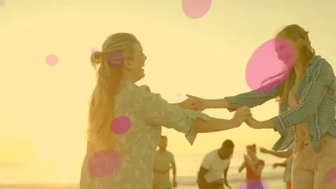 Two women clasping hands, playing and spinning on beach, creating pink-purple Stock Footage 331123685