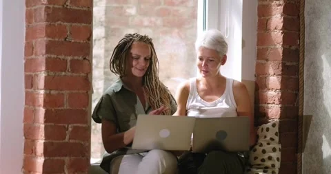 Two women concentrated at work, working on laptop, talking while sitting near Stock-Footage 248611144