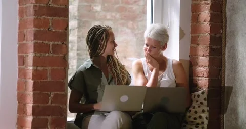 Two women concentrated at work, working on laptop, talking while sitting near Stock-Footage 248863979