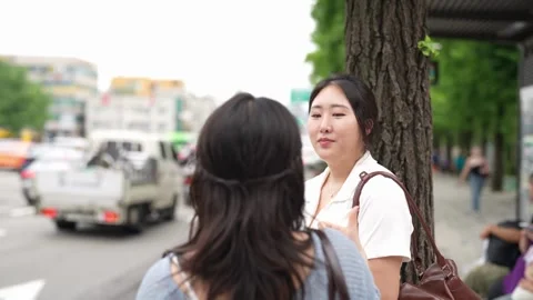 Two women converse beside a tree on a city sidewalk Stock Footage 340929308