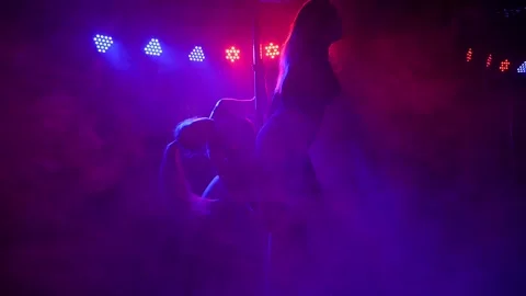 Two women dancing around the pole by the light of colorful lights. Pole dance. Stock Footage 155423915