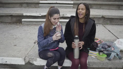 Two women drinking mate cup infusion seated in urban park 库存影片 130432096