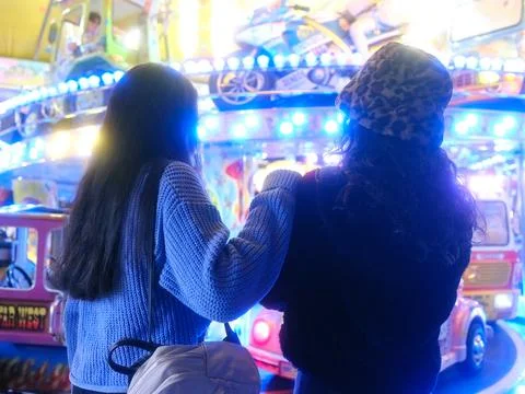 Two women embracing while looking at a carousel in a night fair Stock Photos
