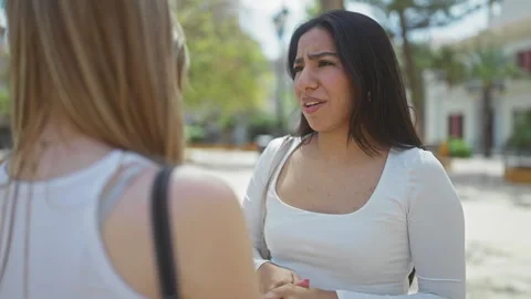 Two women engaging in a friendly conversation outdoors in a sunny urban par.. Stock-Footage 276186950