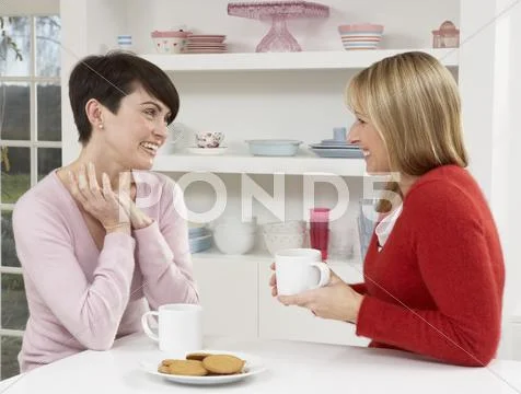 Two Women Enjoying Hot Drink In Kitchen Stock-Fotos