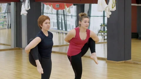 Two women in gym make complex gymnastic exercises standing on one leg. Stock Footage 86565572