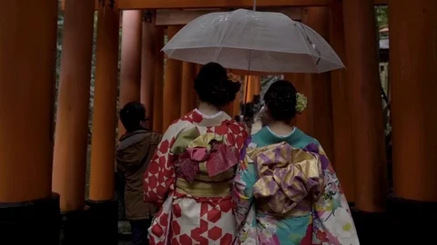 Two women in kimono walking through the Torii gates with an umbrella Stock Footage
