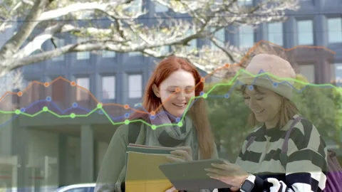 Two women leaning toward tablet, right woman adjusting grip, creating line-chart Stock Footage 334418969
