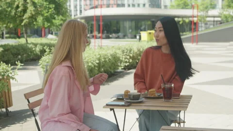 Two Women Looking Away While Sitting At Outdoor Cafe On Sunny City Street 스톡 동영상 318992097