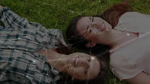 Two women lying on grass, camera pulling back, overlay forming nodes over faces, Stock Footage 330935482