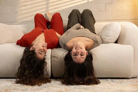 Two women lying upside down on couch laughing Stock Photos