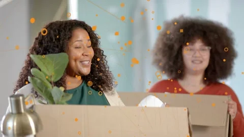 Two women moving boxes, camera zooming in focusing left woman, orange overlay Stock Footage 332841434