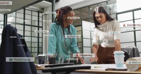 Two women in office discussing documents with data processing animation over Stock Footage 303422563