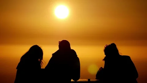 Two women &amp; one man upper body sitting at table silhouette against setting sun Stock Footage 78524495