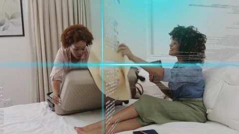 Two women packing suitcase for travel on bed, tablet guiding choices while Stock Footage 333368853