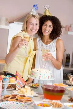 Two women at party holding drinks standing by food table smiling Stock Photos