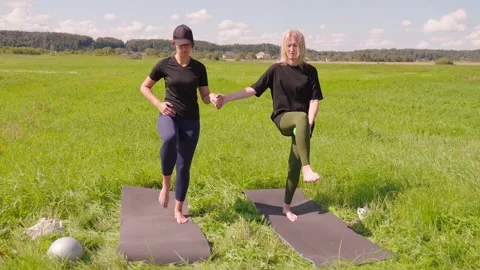 Two women performing balancing exercises holding hands in a field Vídeo Stock 329475955